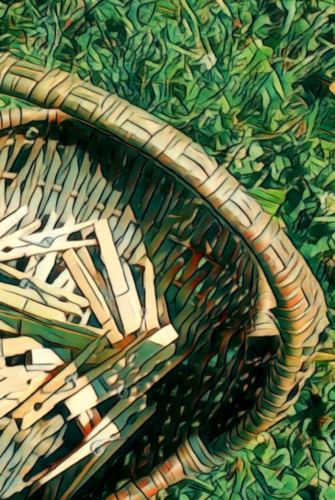 An artfully altered photo of a reed basket sitting on green grass, half-filled with wooden clothespins.